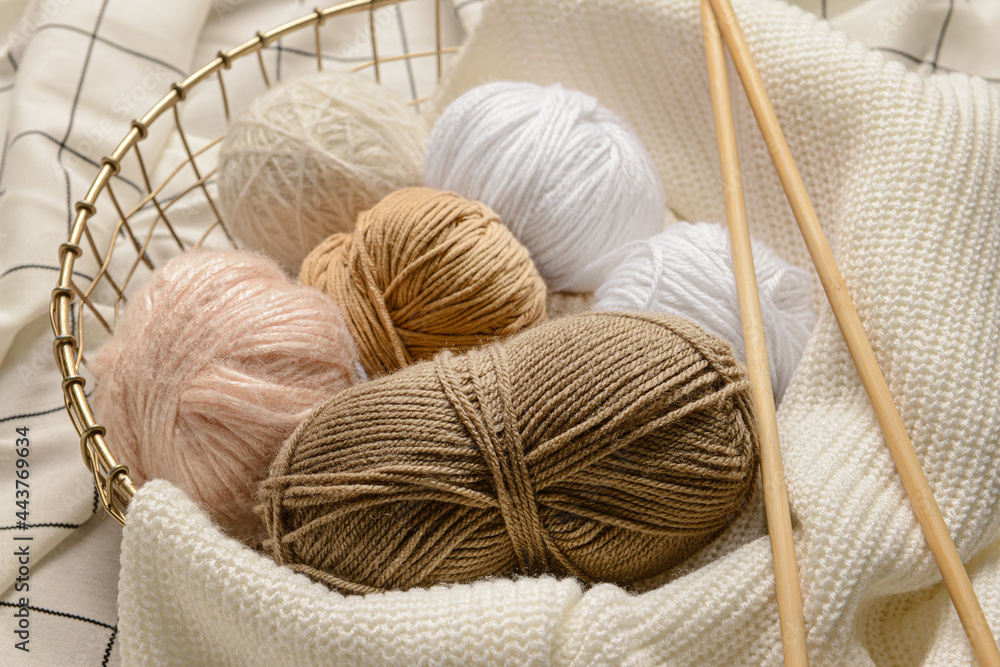 Basket with knitting yarn and needles on fabric background, closeup