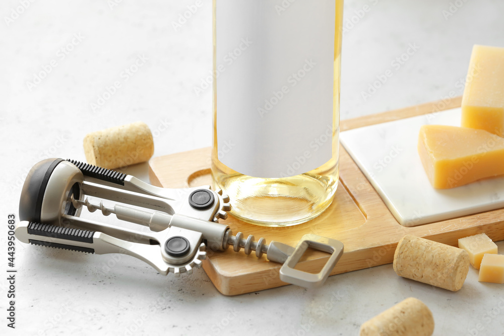 Wooden board with bottle of exquisite wine, corkscrew and cheese on light table