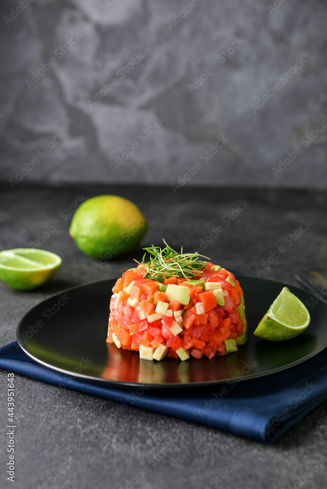 Plate with tasty tartare salad and lime on dark background