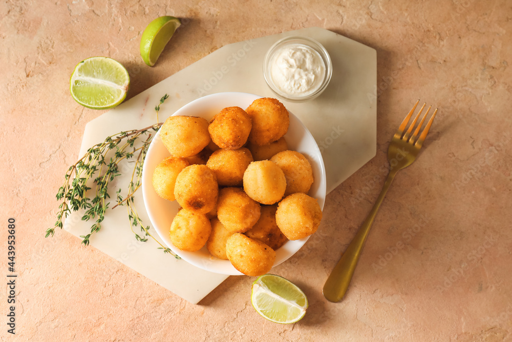 Bowl with fried potato balls and sauce on color background