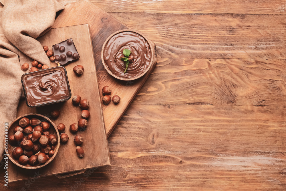 Bowl with tasty chocolate paste and hazelnuts on wooden background