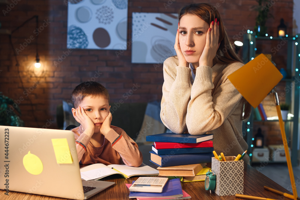 Little boy with his mother tired of doing homework at home late in evening