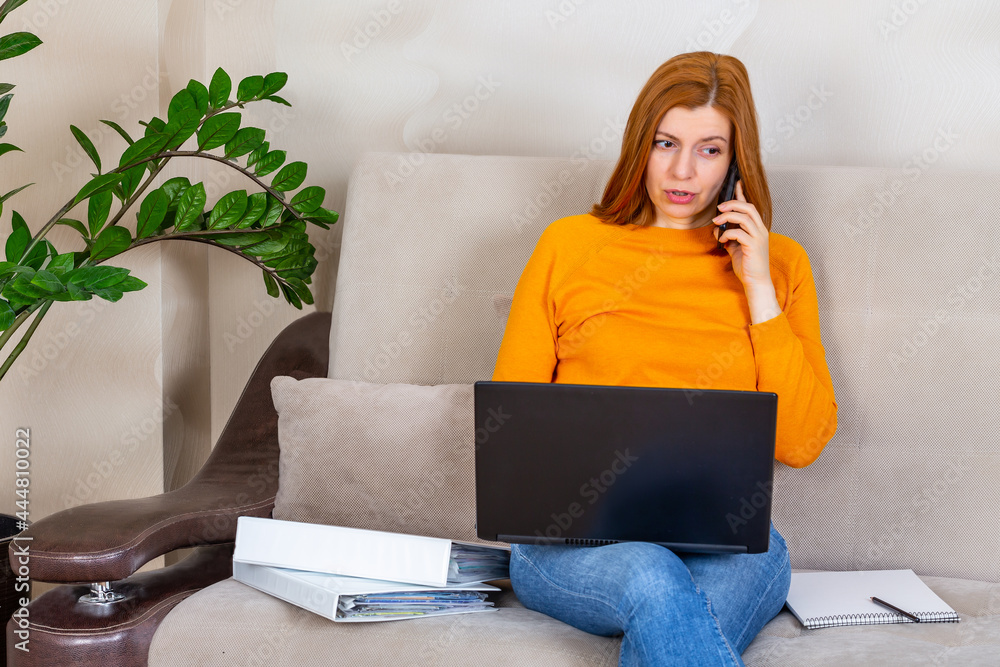 Female freelancer talking by phone and working on laptop at home