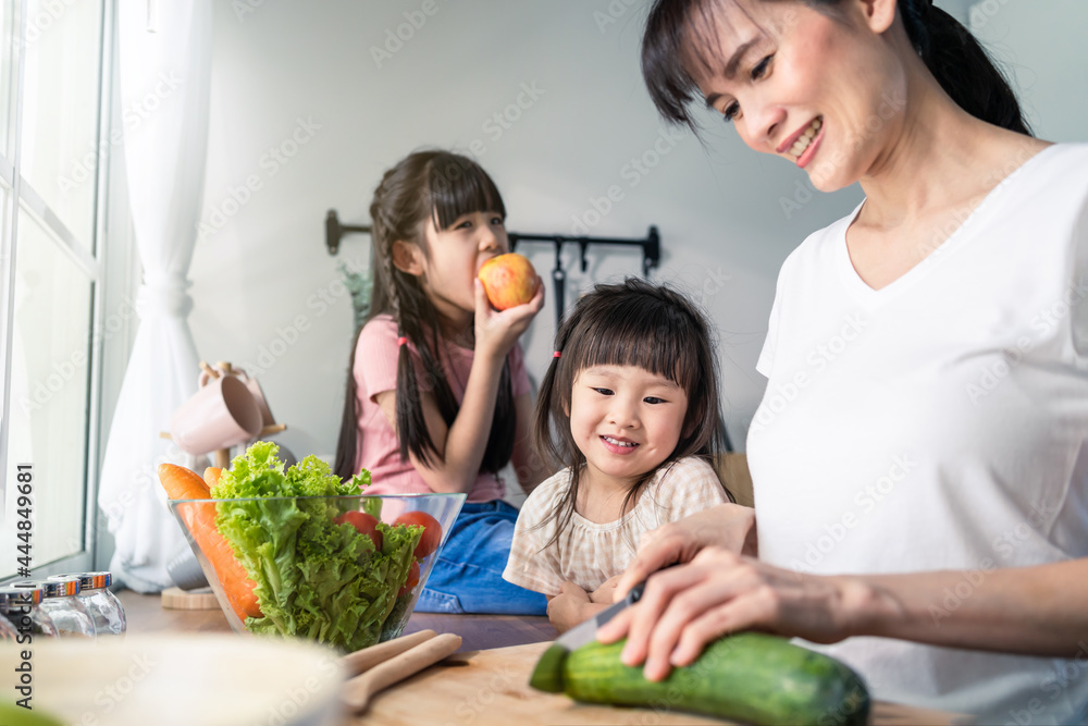 亚洲美女妈妈和两个年幼的女儿一起做蔬菜沙拉