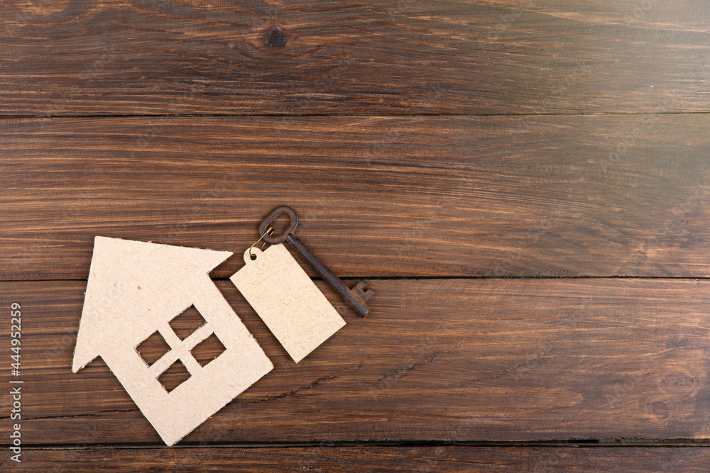 Real estate concept -Buying,selling or rent a house. Old key with tag and cardboard house on wooden 