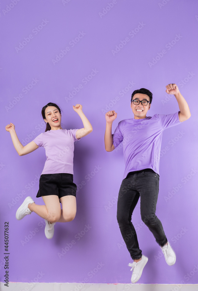 Young Asian couple jumping on purple background