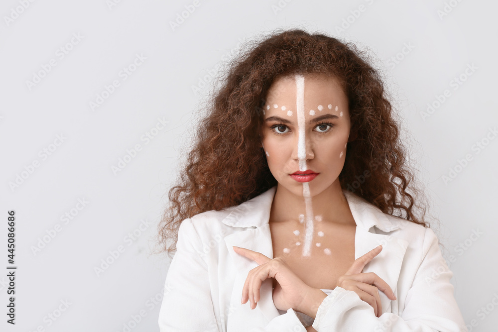 Beautiful young African-American woman with paint on her body against light background