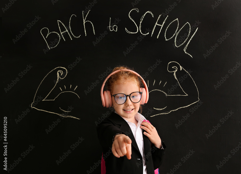 Cute little schoolgirl near blackboard in classroom