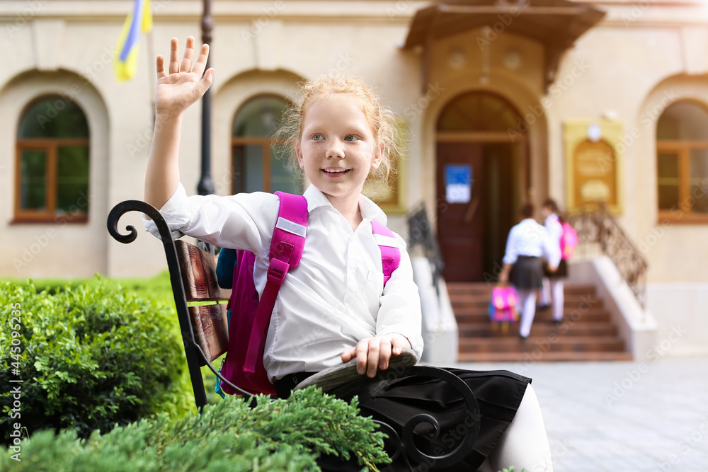 Cute little schoolgirl sitting on bench outdoors