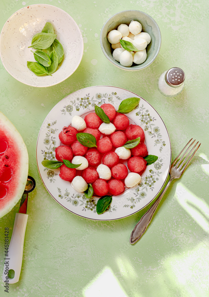 Watermelon salad with mozzarella cheese and fresh basil leaves on green background. Caprese salad wi