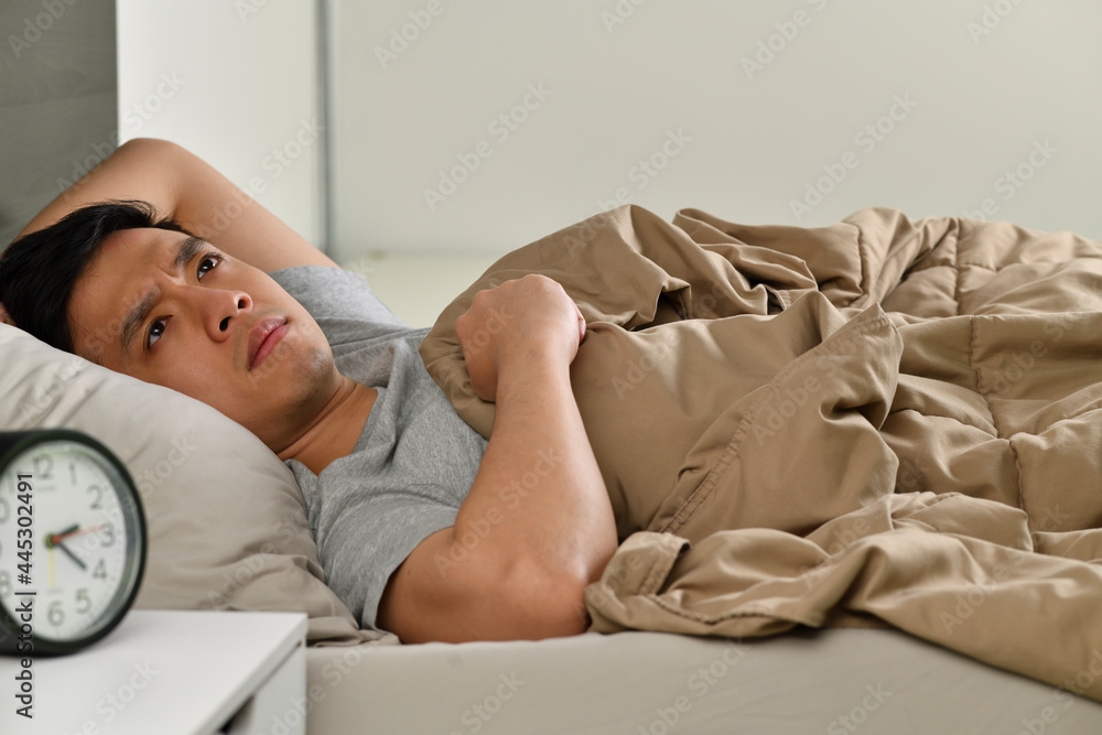 Depressed young Asian man lying in bed cannot sleep from insomnia