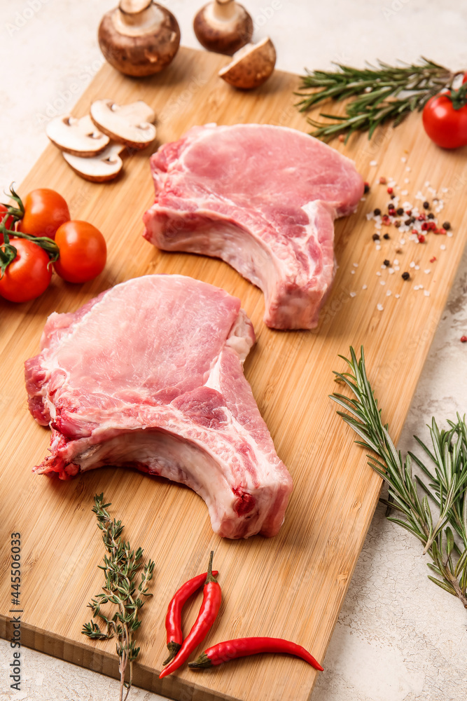 浅色背景上有生猪肉、香料和蔬菜片的木板