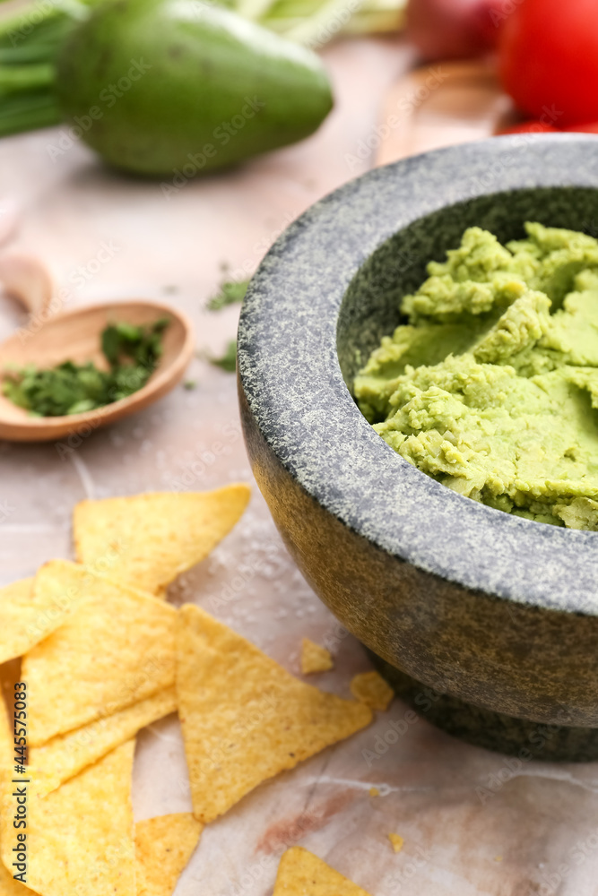 Mortar with tasty guacamole and nachos on color background, closeup