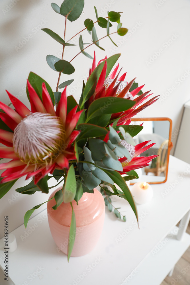 Shelf with protea flowers and mirror near light wall, closeup