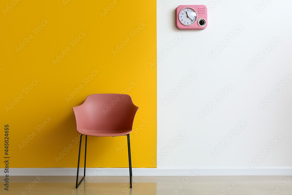 Modern armchair and clock hanging on color wall in room