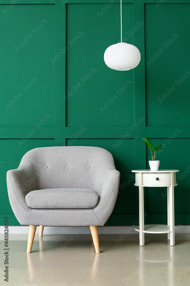 Cozy armchair and table with houseplant near color wall