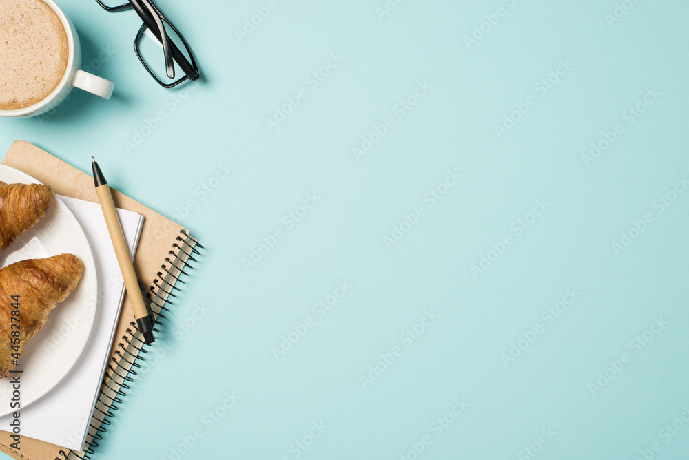 Top view photo of workplace glasses cup of frothy coffee pen planners and plate with two croissants 