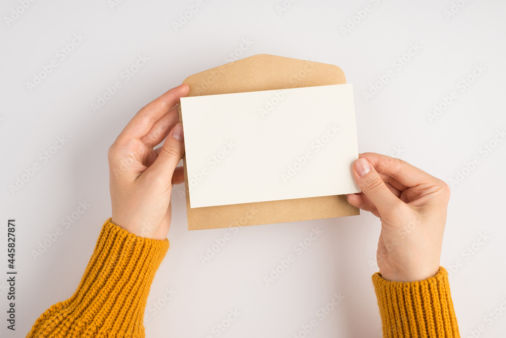 First person top view photo of female hands in yellow sweater holding open craft paper envelope and 