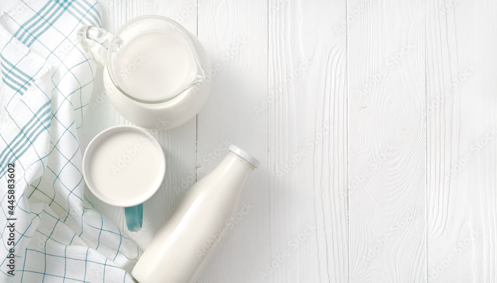 Milk in mug and jug of milk and napkin on white wooden table. Top view flat lay. Bottle of milk on w