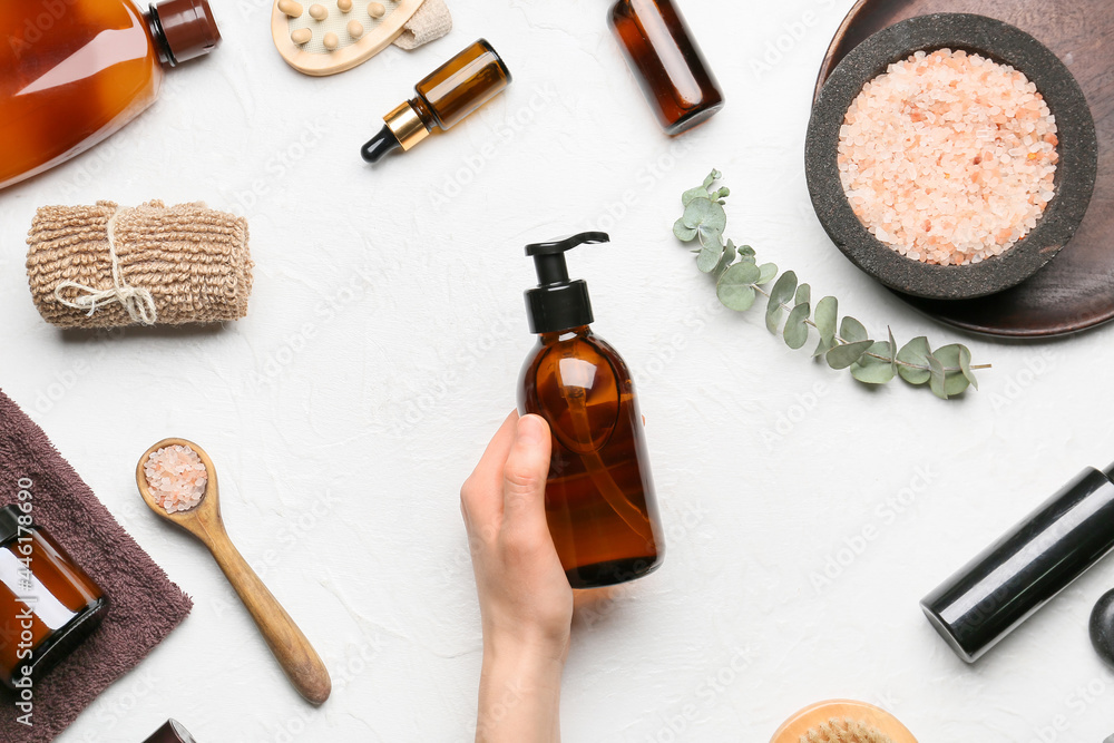 Female hand with bottle of cosmetic product and bath supplies on light background