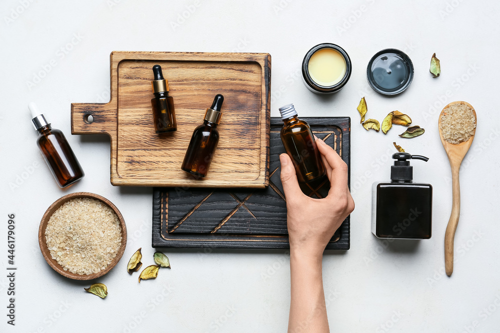 Female hand with different cosmetic products and sea salt on light background