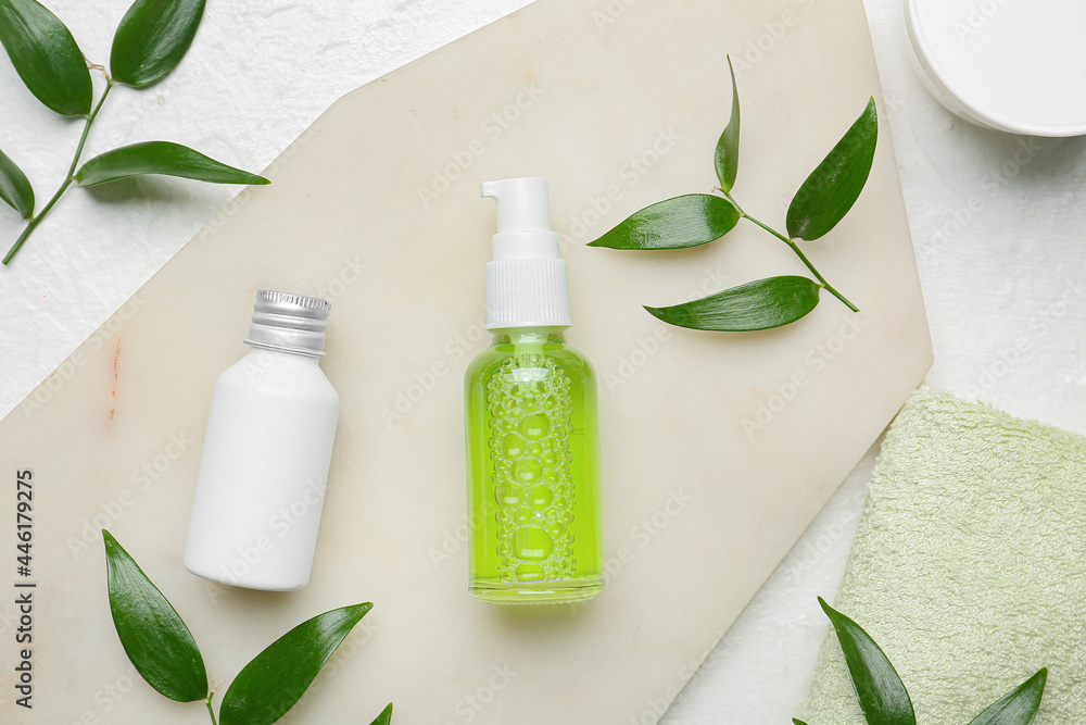 Board with bottles of cosmetic products and leaves on light background