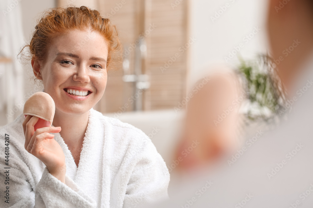 Beautiful young woman applying makeup in bathroom