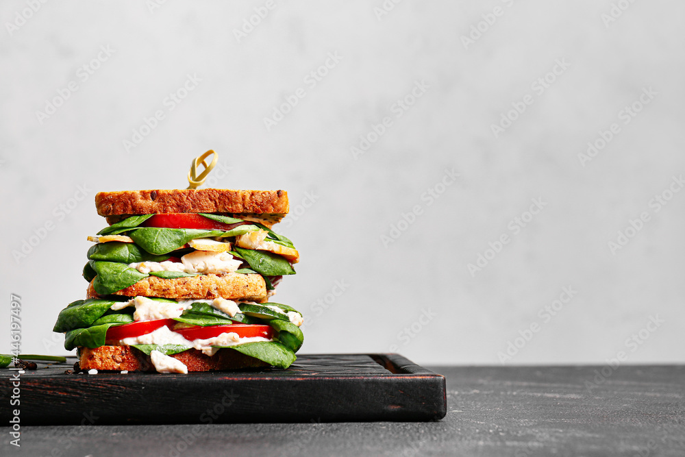 Board with tasty sandwich on light background