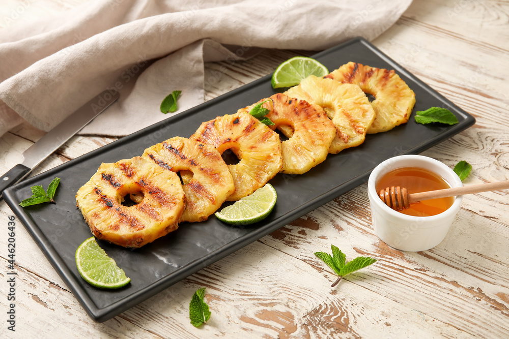 Board with grilled pineapple slices and honey on light wooden background