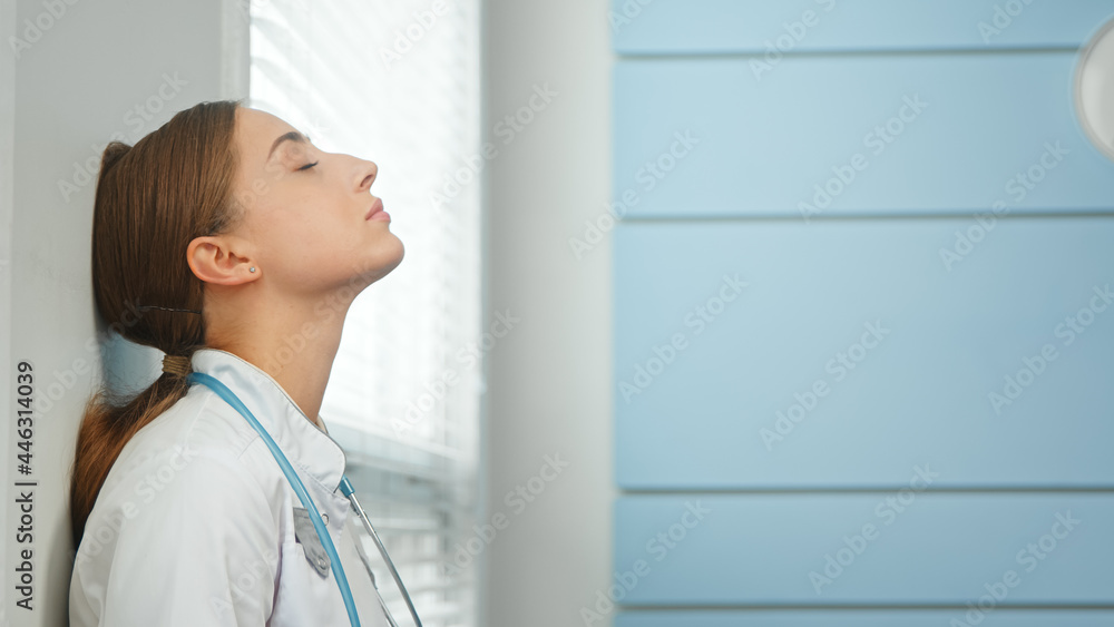 Young woman doctor breathes deeply leaning on wall