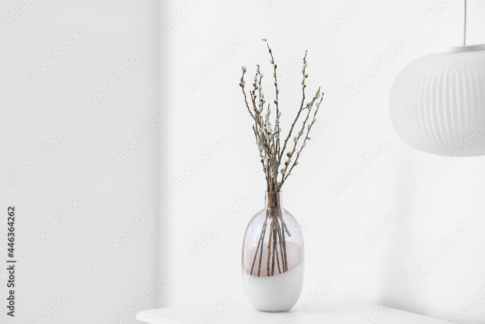 Vase with willow branches on table in room