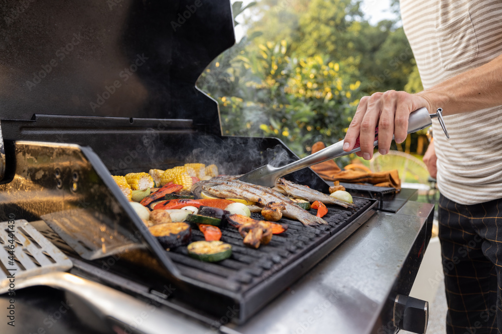 People grilling fish and corn on a modern grill outdoors at sunet, close-up. Cooking food on the ope