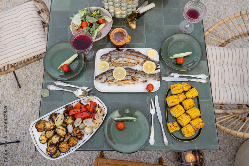 Top view on a beautifully served table with grilled vegetables and fish decorateed with field flower