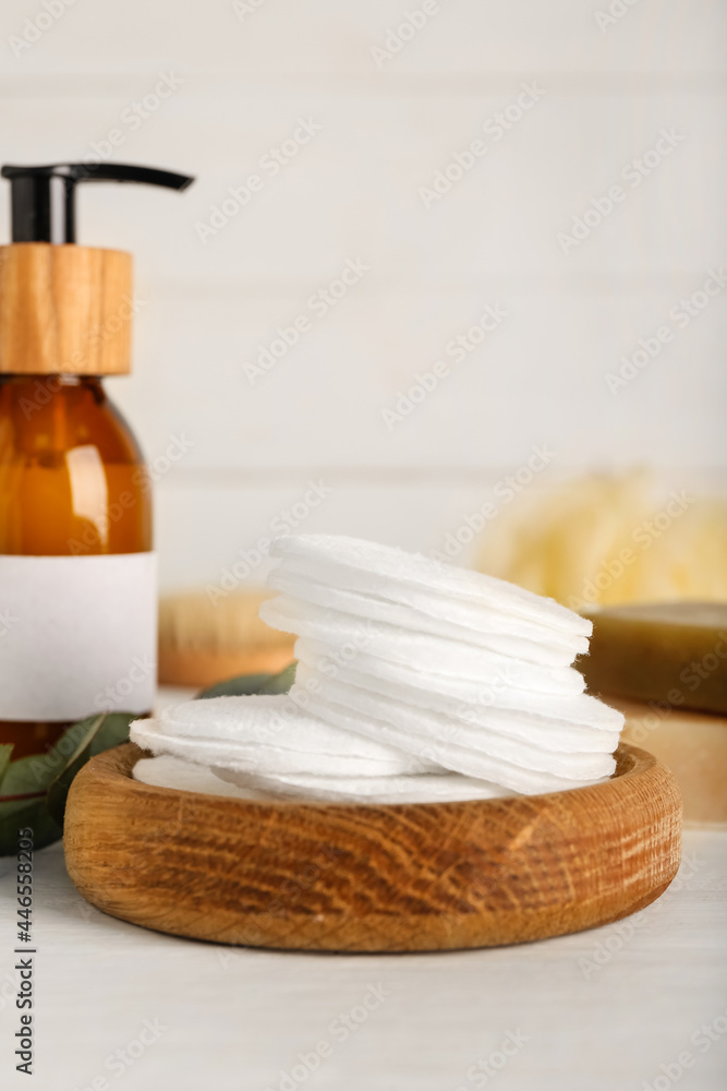 Holder with cotton pads and bottle of cosmetic product on light background, closeup