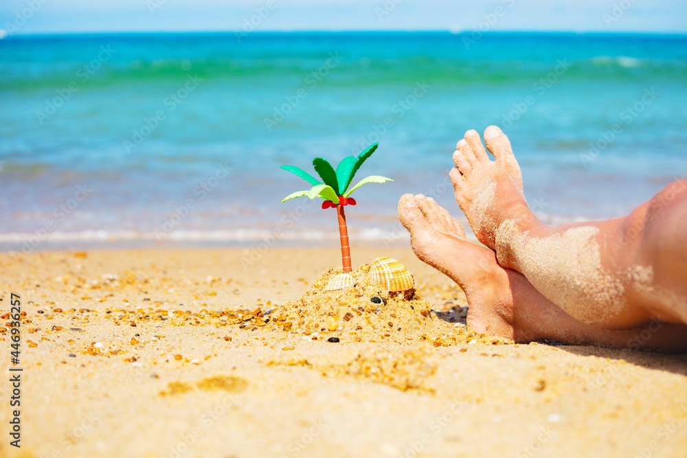 Miniature palm and girls legs in sand close-up