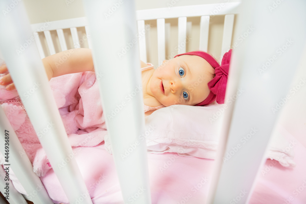 Baby girl in a bed with pink bow look through bars