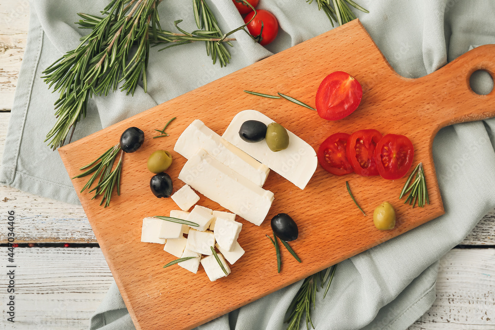 Board with delicious pieces of feta cheese on white wooden background