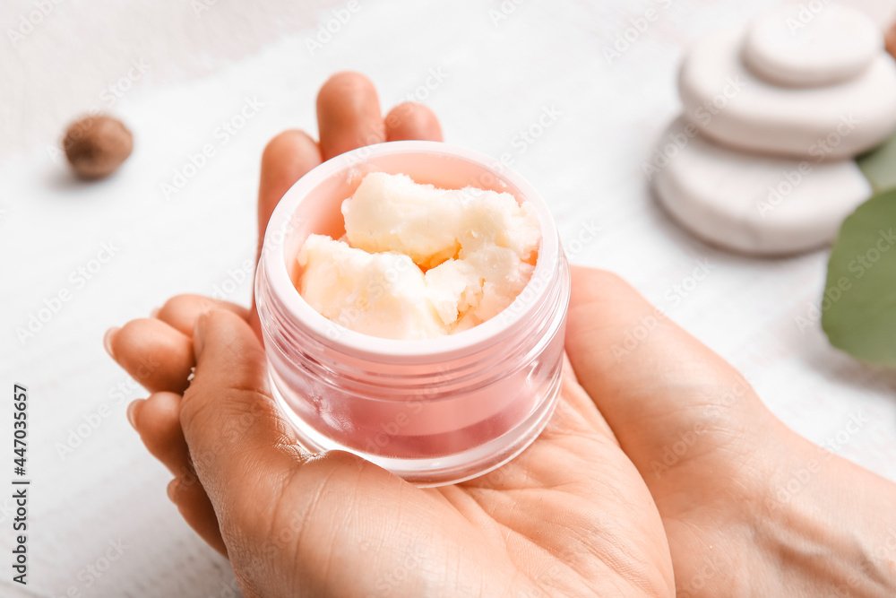 Woman holding jar of shea butter on light background, closeup