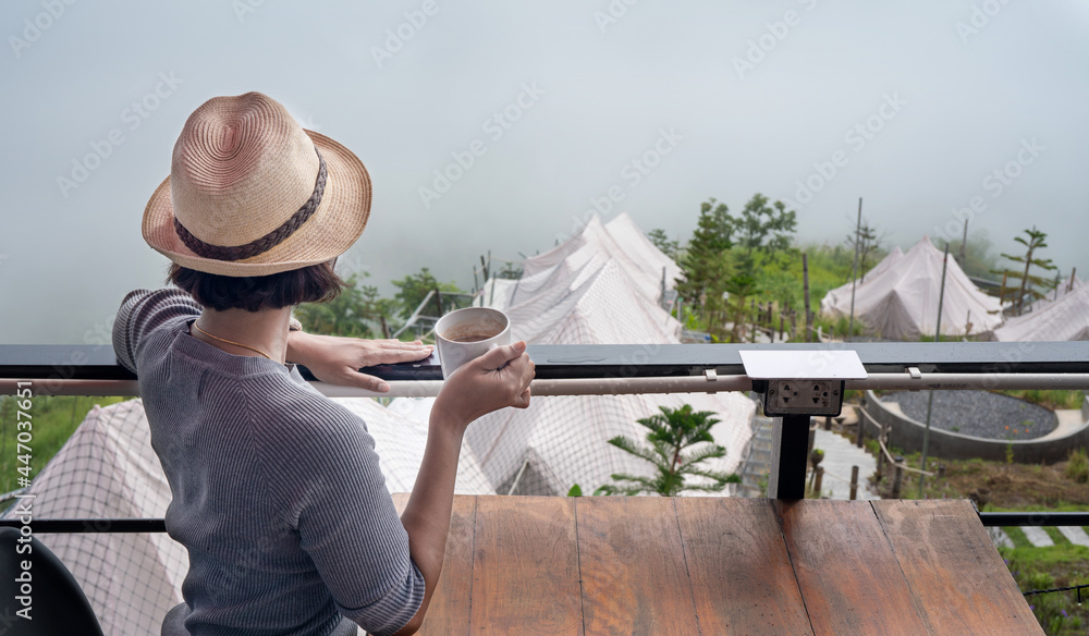 女人拿着一杯卡布奇诺咖啡游览山景。