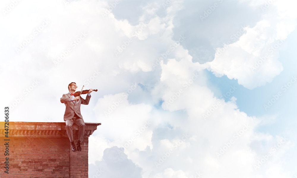 Handsome violinist in glasses on building edge play his melody