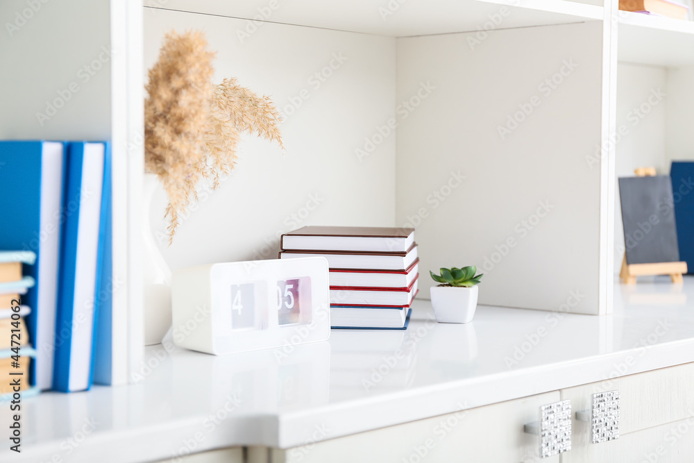 Shelf unit with books, clock and houseplant, closeup