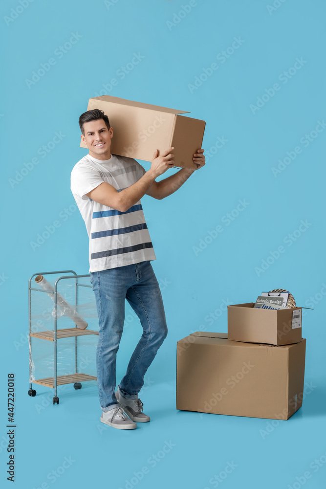 Handsome man with moving boxes on color background