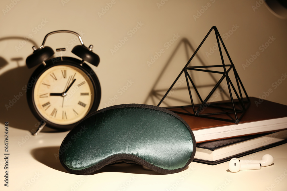 Stylish sleeping mask, earphones, clock and notebooks on color background