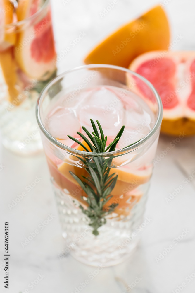 Glass of tasty grapefruit lemonade with rosemary on light background, closeup