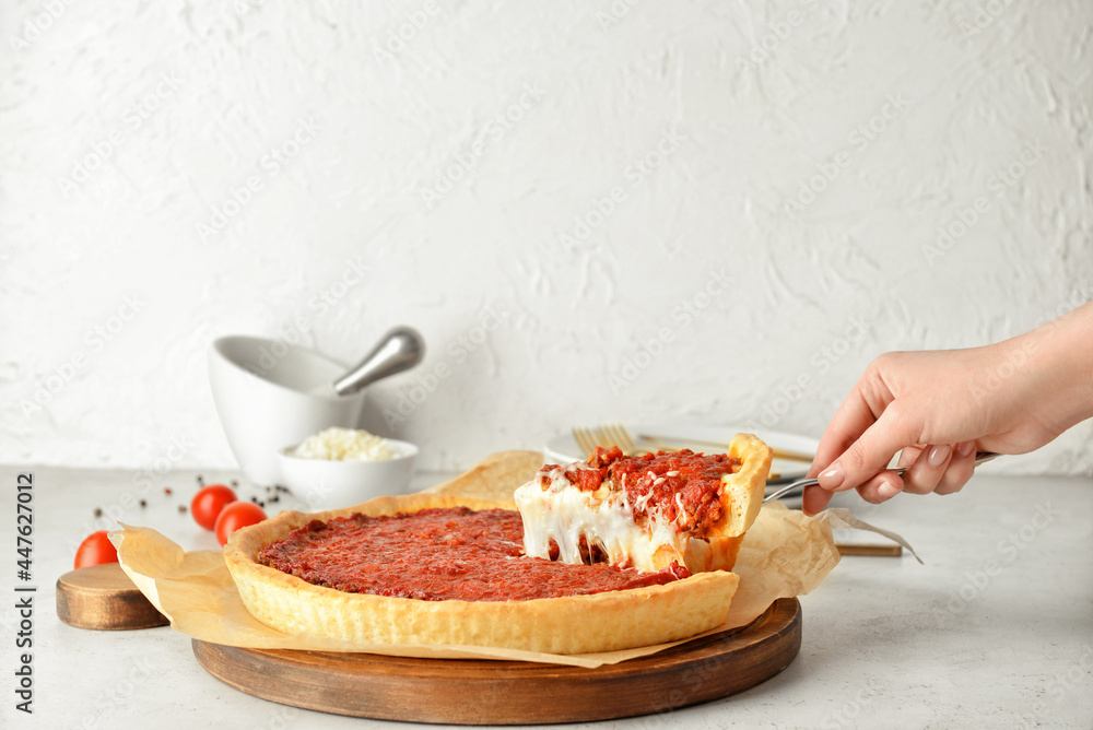 Woman taking piece of tasty Chicago-style pizza on light background