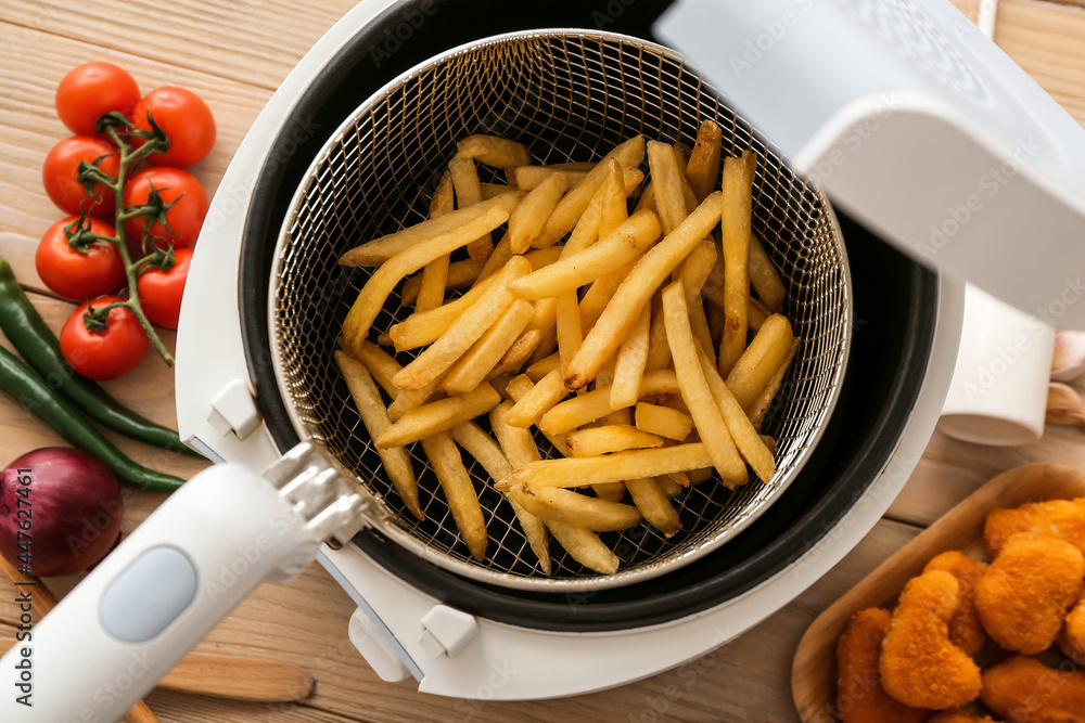 Modern deep fryer with tasty french fries on wooden table, closeup