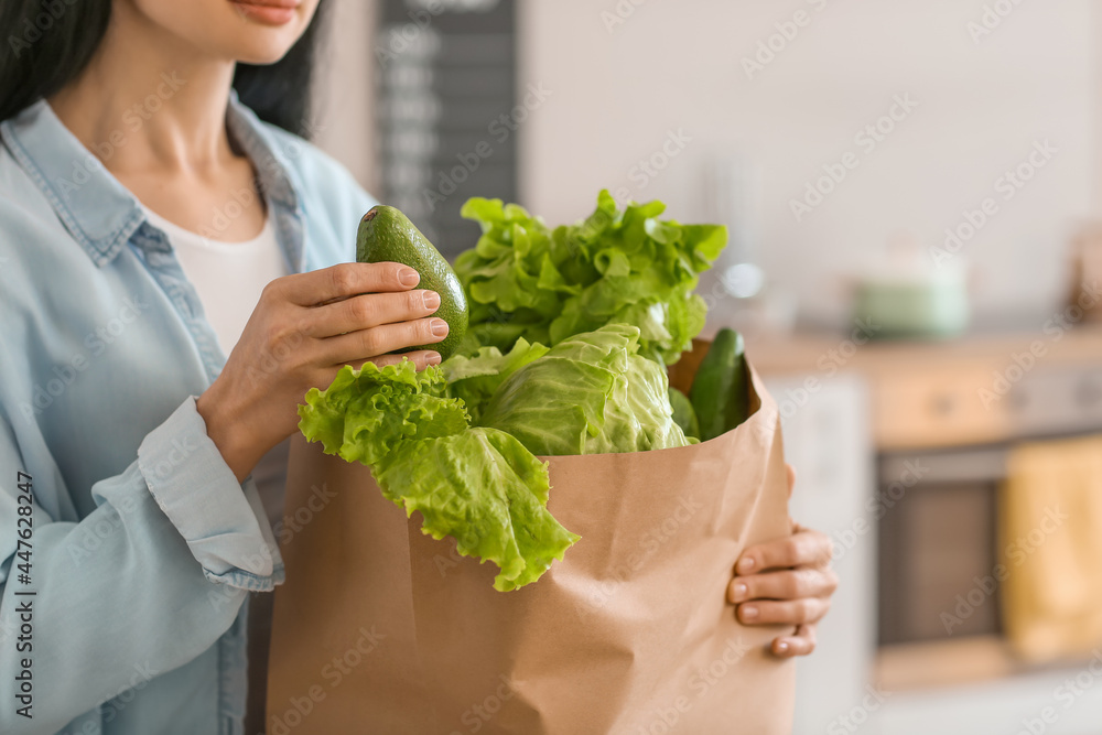 Young woman holding paper bag with fresh vegetables in kitchen