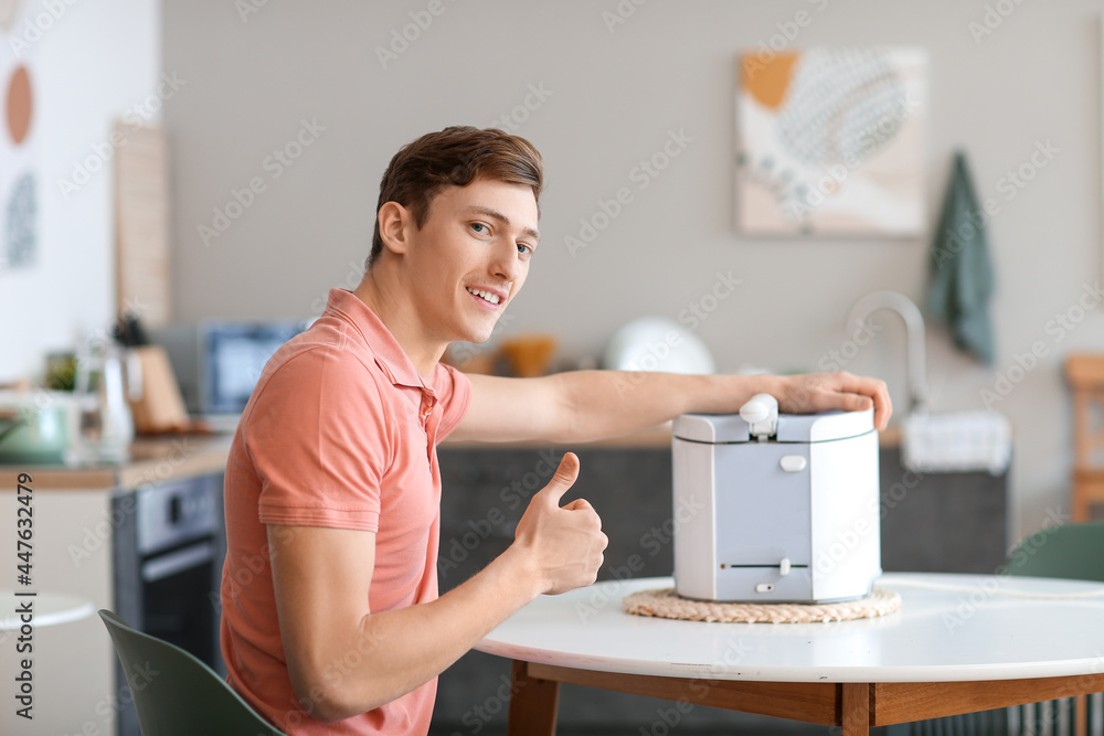 Young man with modern deep fryer showing thumb-up in kitchen