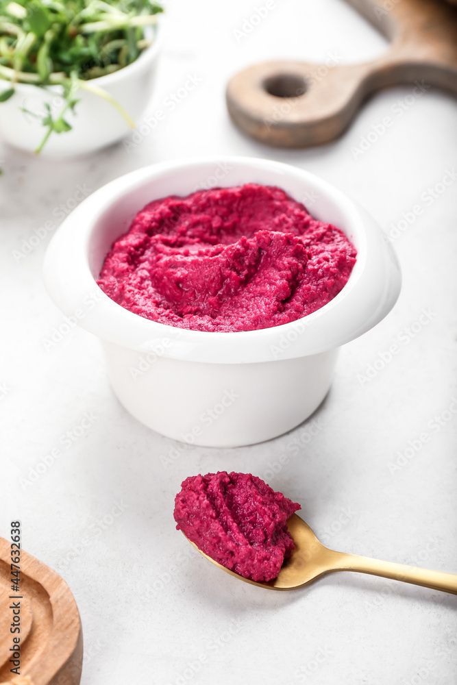 Bowl and spoon  with tasty beet hummus on light background