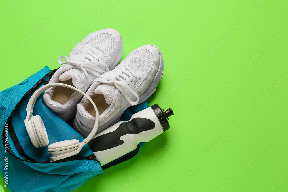 Backpack with sport shoes, bottle of water and headphones on color background